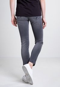 Szare dopasowane dżinsy z wyblakłym wzorem, postrzępionym dołem i tylnymi kieszeniami. Połączone z białymi trampkami, widok z tyłu.