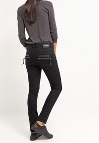 Černé džíny z denimu s úzkým střihem, vybavené kapsami na zip a texturovaným pasem. Kombinovány s dlouhým šedým topem a černými teniskami.