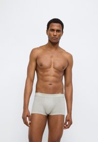 Calzoncillos bóxer de algodón gris con una cintura suave que muestra el logo de "Calvin Klein". El modelo está de pie, mostrando un diseño ajustado.