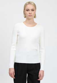 Top lungo a maniche lunghe bianco a costine realizzato in un tessuto elasticizzato con scollatura rotonda. La vestibilità è aderente al corpo e la texture è liscia.