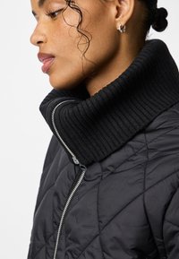 Mustrist musta fliisjakke, millel on paks soonikkoonus ja hõbedane tõmblukk, esitleb sujuvat tekstuuri ja katkematut disaini.