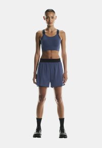 Marineblå sports-bh med tykke stropper, parret med marineblå shorts med elastisk talje. Modellen har sorte ankelsokker og løbesko på.