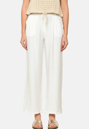 Pantaloni bianchi leggeri con una texture stropicciata, dotati di due tasche laterali e un design rilassato a gamba larga. Il modello indossa un top beige e sandali.