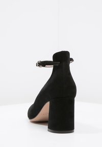 Schwarzer Wildleder-High-Heel-Schuh mit einem robusten Absatz und Knöchelriemen. Die Rückseite hat ein geschlossenes Design mit einer glatten, matten Oberfläche.