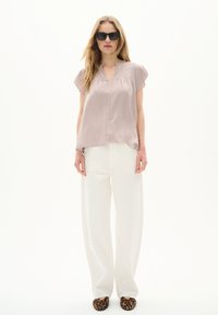 Blusa rosa chiaro a maniche corte con scollo a V. Abbinata a pantaloni bianchi larghi e ballerine con stampa leopardata. La modella indossa occhiali da sole scuri.