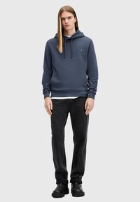 Dark blue sweatshirt with a hood, featuring a kangaroo pocket and ribbed cuffs. Paired with black jeans and black boots. Simple design.