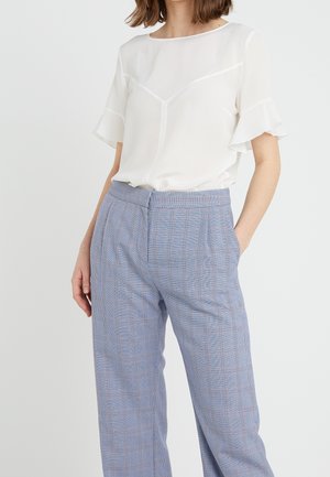 Blusa bianca in chiffon con maniche a volant, abbinata a pantaloni a quadri azzurri chiari con un leggero motivo a scacchi e tasche laterali.