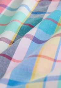 Blødt stof med farverigt pastelternet mønster med krydsende linjer i blå, pink, gule og grønne nuancer, der viser bløde folder.