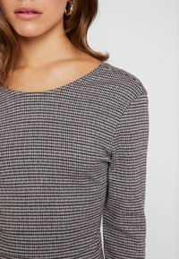 Grå och svart mönstrad topp med rundad halsringning och långa ärmar, som har en strukturerad tyg och en figurnära design.