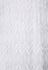 Tissu en dentelle blanche avec des motifs horizontaux répétés de formes florales et ovales créant un motif délicat et texturé.