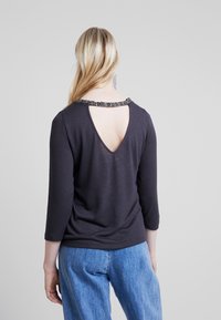 Mörkgrå långärmad topp med V-rygg, prydd med en dekorativ svart pärlhalsringning. Mjuk textur, figurnära passform och en avslappnad design.