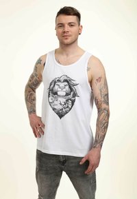 Hvid bomulds tanktop med et detaljeret sort grafik af en løve inden i en hjerteform, båret sammen med slidte grå jeans.