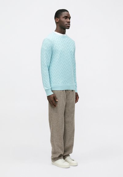 Sweat-shirt tricoté bleu clair avec un motif texturé, col blanc, associé à un pantalon large gris et des baskets blanches.