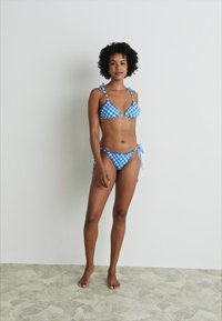 Ensemble de bikini à carreaux bleu et blanc comprenant un haut triangulaire avec des liens aux épaules et un bas taille basse avec des liens sur les côtés. Texture lisse.