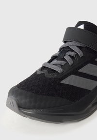 Mustad spordijalats, mille pealmine osa on võrgust, hallide paelte ja takjakinnitusega; külgedel on kolm halli triipu ning tekstuuriga kummist tallaga.