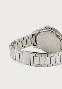 Montre en acier inoxydable argenté avec un bracelet à maillons, un boîtier rond et une finition polie. Comprend un fermoir avec un détail de logo.