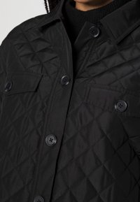 Black quilted jacket featuring a button-up front, two chest pockets, and a textured pattern with visible stitching and black buttons.