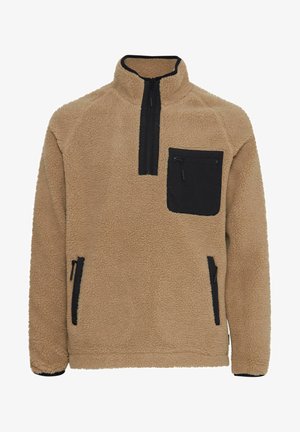 Bēša flīsa džemperis ar augstu apkakli, melnu rāvējslēdzēja krūšu kabatu un melnām akcentētām rāvējslēdzējām uz kabatām. Mīksta tekstūra visā džempera virsmā.