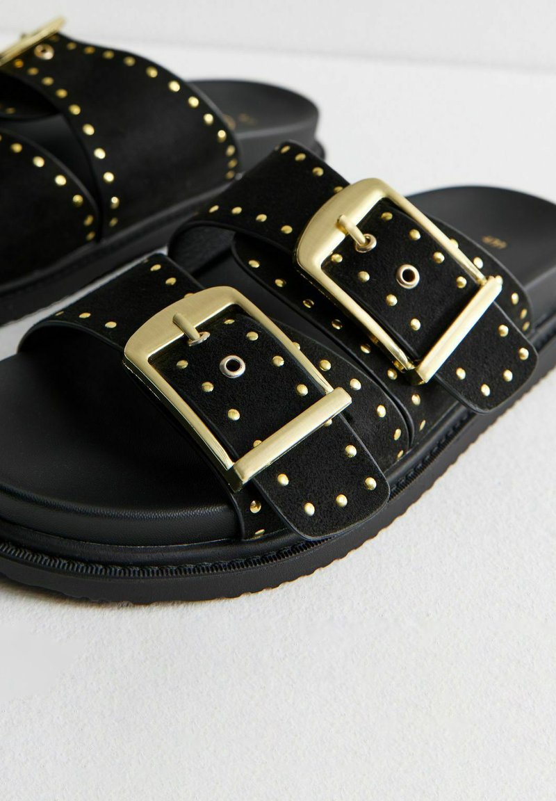 Sandalias negras con dos correas anchas, adornadas con tachuelas doradas. Las hebillas también son doradas. Material de ante texturizado y plantilla acolchada.