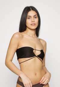 Bralette preta sem alças com um design franzido e detalhe torcido à frente. Feita de um material suave, com laços ajustáveis para melhor ajuste.