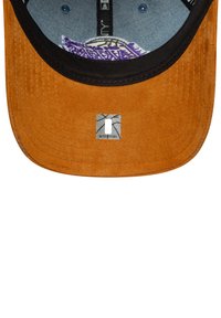 Casquette de baseball avec un extérieur en daim marron, une visière noire et un intérieur en denim. Présente une étiquette rectangulaire avec un design graphique.