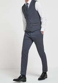 Dopasowany szary garnitur z kamizelką, biała koszula, guziki z brązowymi akcentami, spodnie o wąskim kroju i czarne buty. Gładka tekstura, nowoczesny design.