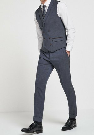 Op maat gemaakt grijs vestpak met een wit overhemd, knopen met bruine accenten, slim-fit broek en zwarte schoenen. Glad oppervlak, modern ontwerp.