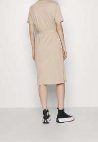 Beige puuvillainen midi-mekko, jossa on lyhyet hihat ja sidottu vyötärö, yhdistettynä mustiin korkeisiin tennareihin, joissa on valkoisia yksityiskohtia.