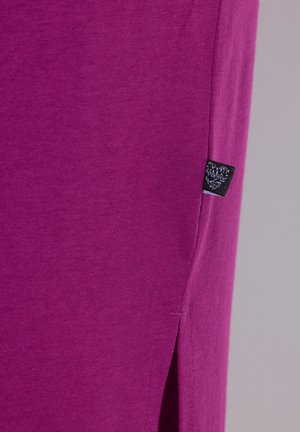 Lähikuva violetista kankaasta, jossa on sivusauma ja pieni musta vaatetunniste lähellä sivuhalkiota.