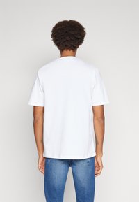 T-shirt bianco a maniche corte con scollo rotondo, realizzato in tessuto di cotone morbido. Presenta una vestibilità comoda e la vista posteriore mostra un design semplice.