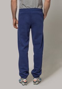 Tummansinisiä collegehousuja, jotka on valmistettu pehmeästä kankaasta. Housuissa on rento istuvuus, joustava vyötärönauha ja nilkassa resorit, joita on yhdistetty urheilukenkien kanssa.