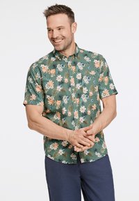 Camicia a maniche corte floreale in tessuto verde con fiori bianchi, arancioni e blu, caratterizzata da un colletto classico e abbottonatura frontale.