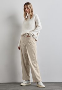 Beige wijde broek in combinatie met een licht crèmekleurige gebreide trui. Textuurstof met een ontspannen pasvorm. Witte sneakers maken de outfit compleet.