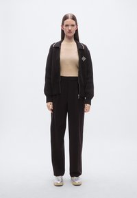 Cardigan noir tricoté avec bordure blanche, haut côtelé beige, et pantalon noir ample. Chaussures argentées avec semelle épaisse et détail zippé.