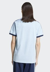 Camiseta de algodón de color azul claro con acentos en azul marino en las mangas y los hombros; ajuste relajado, mangas cortas y un diseño sencillo.