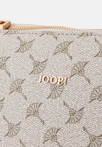 Υφασμάτινη μπεζ θήκη με γεωμετρικό σχέδιο φύλλου, διαθέτει χρυσή φερμουάρ και λογότυπο. Συμπαγής σχεδίαση κατάλληλη για αξεσουάρ.