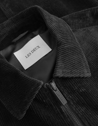 Μαύρο τζάκετ από κορντούρα με απαλή υφή, που διαθέτει φερμουάρ και μια ετικέτα που γράφει "LES DEUX" μέσα στον γιακά.