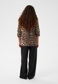 Camicia con stampa leopardata e maniche lunghe, tessuto testurizzato. Abbinata a pantaloni neri a gamba larga, che mostrano un fit rilassato.