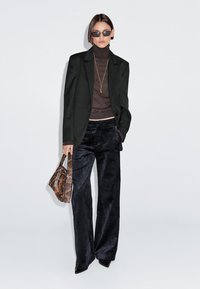 Zwarte blazer over een bruine coltrui, gecombineerd met marineblauwe wijde corduroy-broeken. Accessoires zijn onder andere een zonnebril en een gestructureerde bruine handtas.