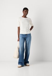Haut en tricot blanc à manches courtes avec un col rond, associé à un jean large bleu clair et un sac à épaule crème. Les chaussures sont de couleur crème avec des semelles beiges.