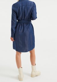 Sukienka koszulowa z denimu w ciemnym niebieskim kolorze, z kołnierzem, długimi rękawami i paskiem w talii. Połączona z beżowymi masywnymi botkami.