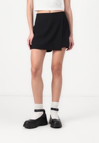 Musthave mustaga, millel on asümmeetriline disain, mis on valmistatud sujuvast kangast. Kombineeritud massiivsete mustade kingade ja valgete soonikkudega sokkidega.