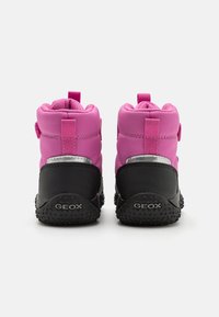 Bottes imperméables roses avec col rembourré, semelle texturée noire et languettes de tirage pour un enfilage facile. Présente le logo de la marque "GEOX" sur le talon.