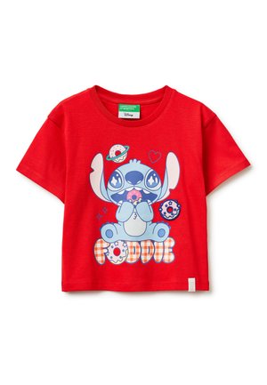 T-shirt rouge pour enfants avec un personnage de dessin animé bleu tenant un donut rose, entouré de donuts et du mot « FOODIE » en lettres à motifs.