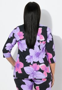 Czarna bluzka z rękawami 3/4, ozdobiona dużymi fioletowymi i różowymi kwiatowymi wzorami. Materiał jest miękki, lekko elastyczny; gładka faktura.