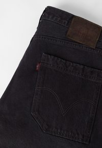 Μαύρα denim τζιν διπλωμένα για να δείξουν την πίσω τσέπη με χαρακτηριστική ραφή και καφέ δερμάτινη ετικέτα μάρκας στη μέση.