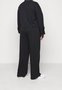 Sudadera negra de gran tamaño con hombros caídos, combinada con pantalones anchos negros. Tejido texturizado y diseño sencillo. Calzado blanco mostrado.