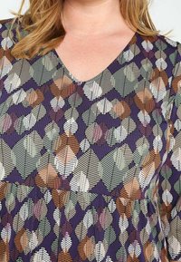 Robe multicolore avec un décolleté en V et des manches courtes. Le tissu présente un motif de feuilles aux tons terreux sur un fond violet foncé.