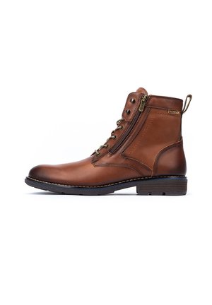 Bottines en cuir marron avec une fermeture éclair sur le côté, bout rond et détails de couture minimalistes. Dotées d'une semelle noire robuste et d'une boucle au talon.
