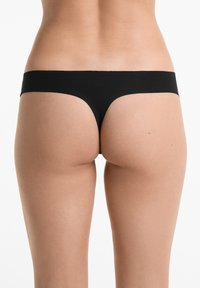 Zwarte stringonderbroek van een gladde, rekbare stof. Kenmerkt zich door een minimalistisch ontwerp met een brede tailleband en geen zichtbare patronen of hardware.